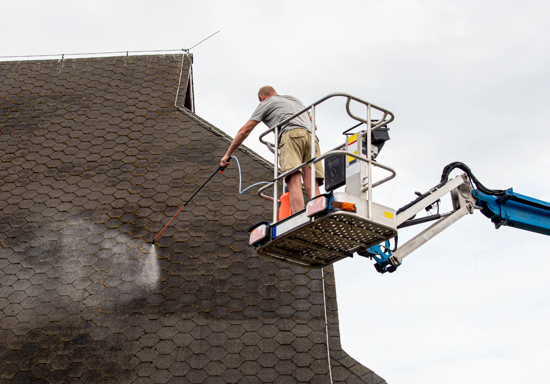 Worker using a pressure washer from a cherry picker to clean the roof tiles