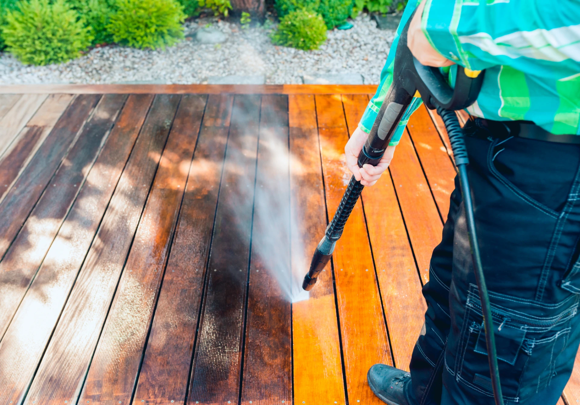 Worker using a pressure washer to clean a wooden deck